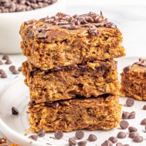 A stack of pumpkin protein bars on a white plate with chocolate chips sprinkled around.