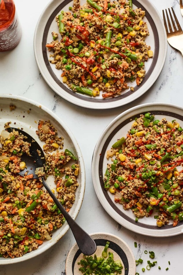 Overhead shot of two plates of quinoa fried rice with a serving bowl of additional quinoa fried rice next to them.