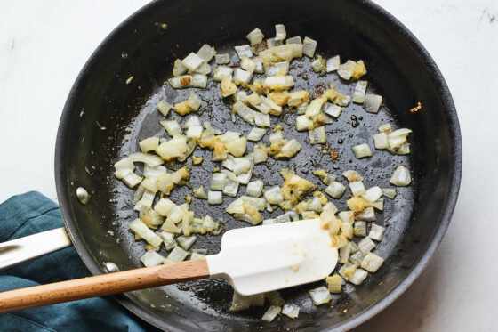 A skillet with sautéed onions and garlic. A spatula rests inside of the skillet.