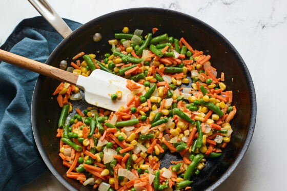 A skillet with vegetables, onion, and garlic. A spatula rests in the skillet.