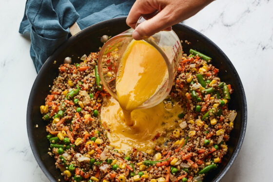 Eggs being added to quinoa and vegetables in a skillet.