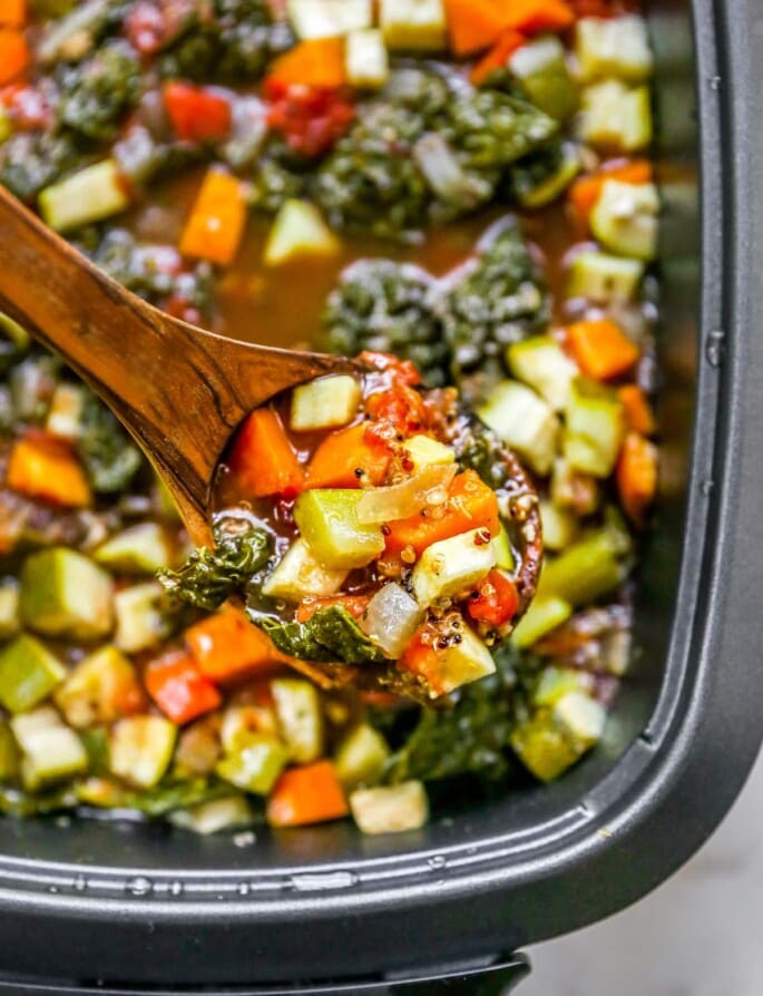 Finished soup in the slow-cooker with a wooden spoon lifting some up.