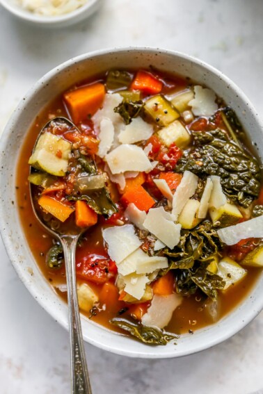 Bowl of quinoa vegetable soup with a spoon lifting some soup out of the bowl.