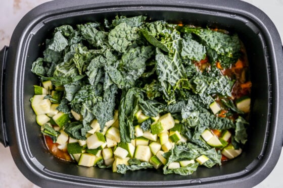 An overhead shot of the slow-cooker with leafy greens added on top.