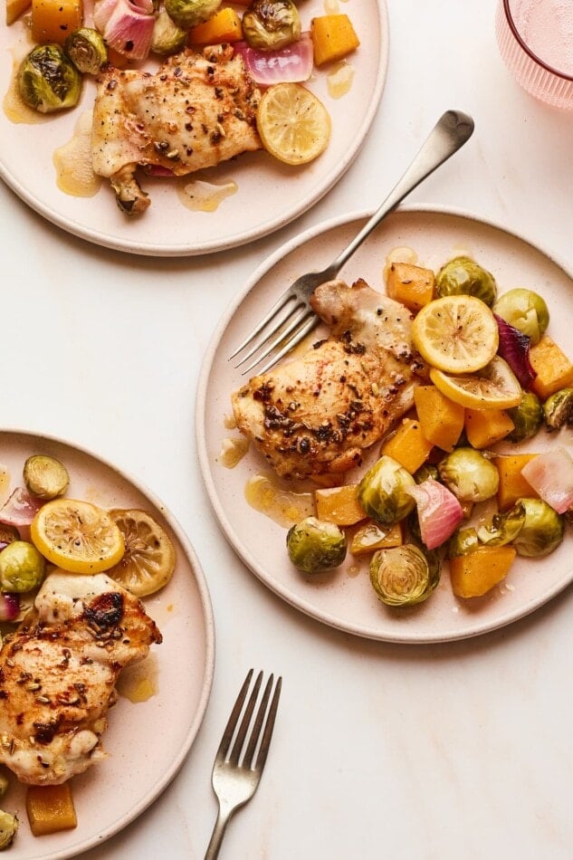 Overhead shot of 3 plates of oven roasted chicken and vegetables. Two of the plates are only half in the frame.