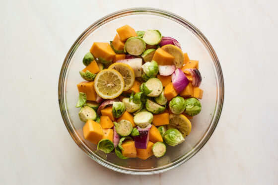 Vegetables and lemon mixed together with oil and seasonings in a glass bowl.