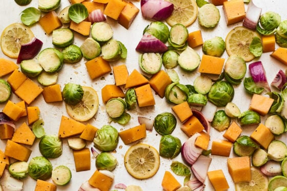 A sheet pan covered with Brussels sprouts, butternut squash, onions, and lemon slices.