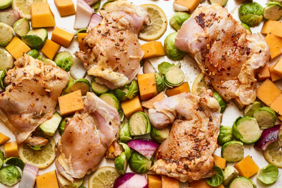 A sheet pan with 5 chicken thighs with roasted vegetables nestled around them.