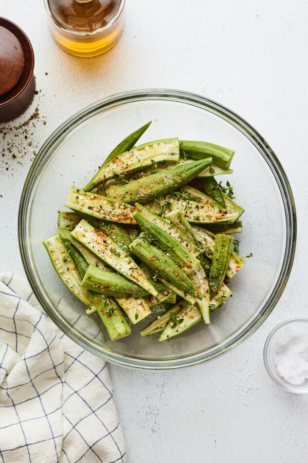 Fresh okra in a mixing bowl seasoned with spices and herbs.