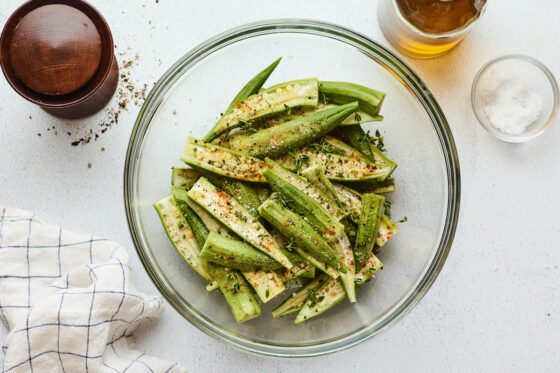 Fresh okra in a mixing bowl seasoned with spices and herbs.