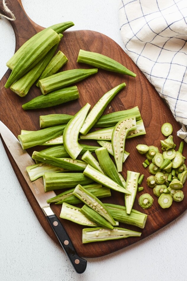 Fresh okra being chopped on a wooden cutting board.