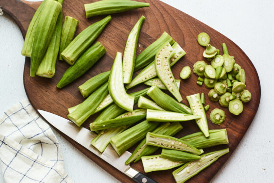 Fresh okra being chopped on a wooden cutting board.