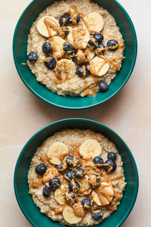 An overhead shot of two bowls of steel cut oatmeal with bananas, blueberries, and almond butter drizzled on top.