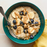 An overhead shot of a bowl of steel cut oats with banana slices, blueberries, and an almond butter drizzle on top.