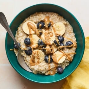 An overhead shot of a bowl of steel cut oats with banana slices, blueberries, and an almond butter drizzle on top.