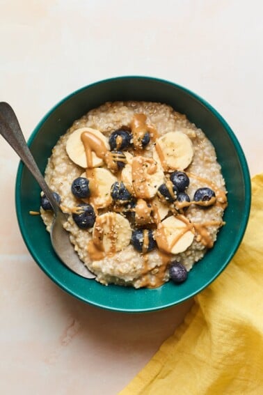 An overhead shot of a bowl of steel cut oats with banana slices, blueberries, and an almond butter drizzle on top.