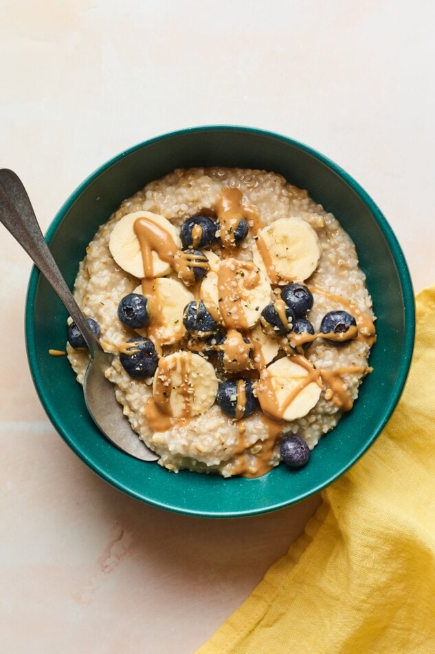 An overhead shot of a bowl of steel cut oats with banana slices, blueberries, and an almond butter drizzle on top.