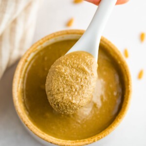 Overhead shot of a hand spooning out some sunflower seed butter from open bowl.