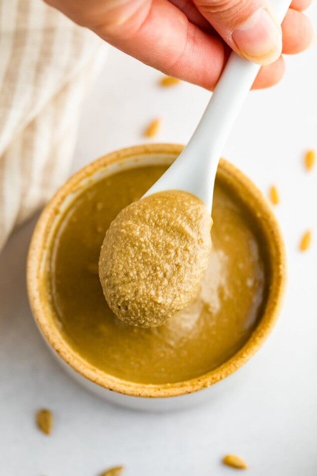 Overhead shot of a hand spooning out some sunflower seed butter from open bowl.