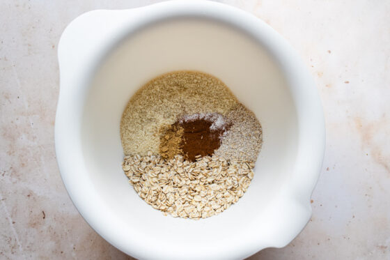 A bowl with oats, processed oats, almond flour, cinnamon, baking powder, salt and ginger ready to be whisked together.