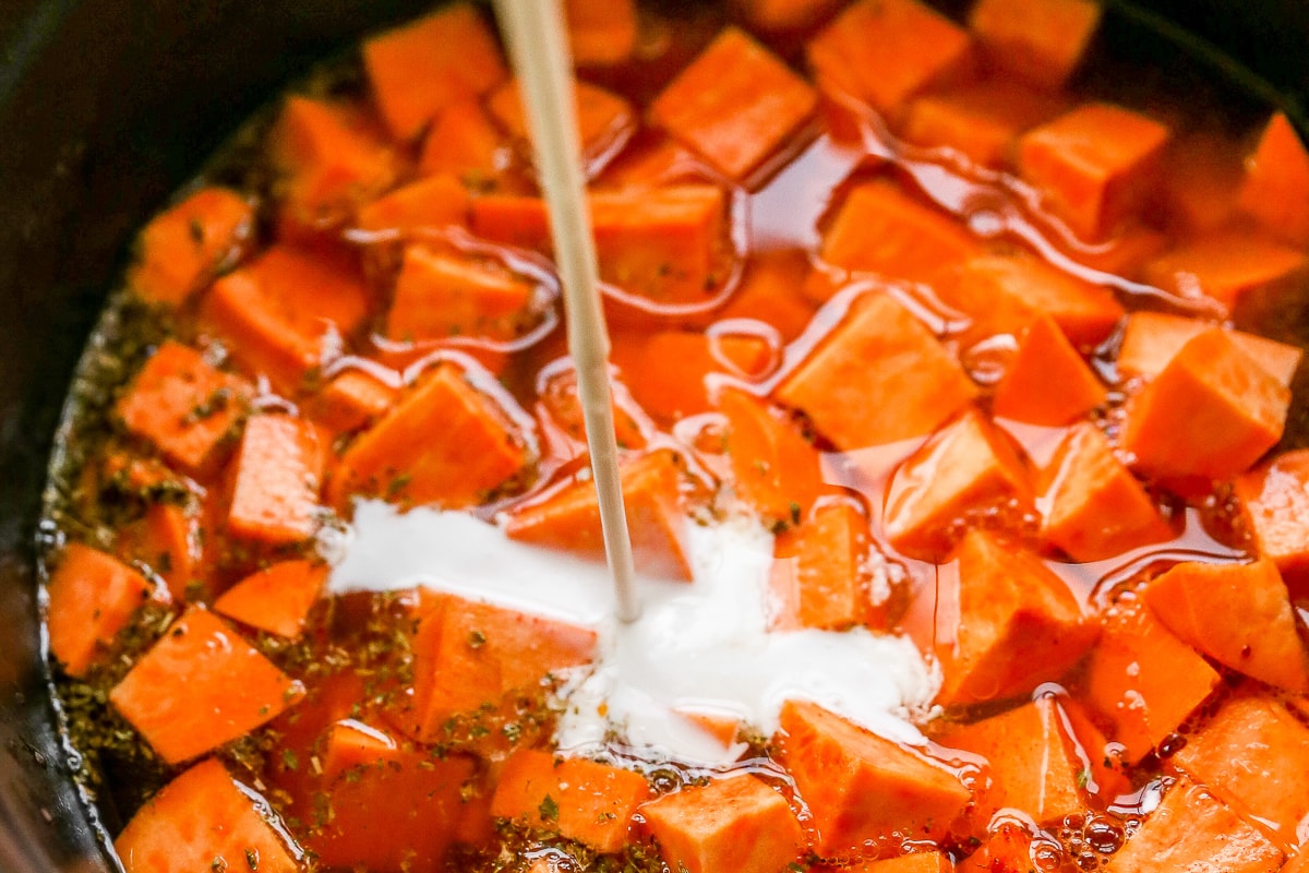 Coconut milk being poured into a pot of soup.