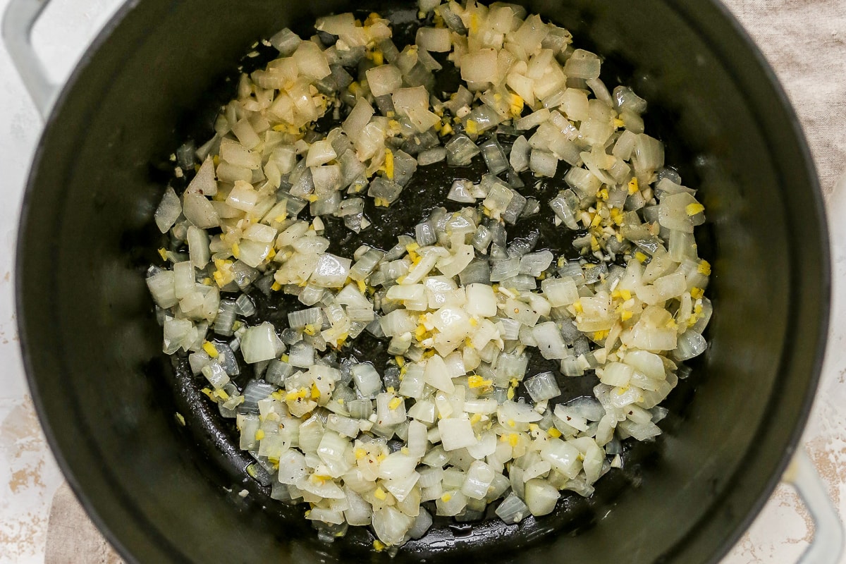 Overhead shot of onions, garlic, and spices in bottom of large pot.