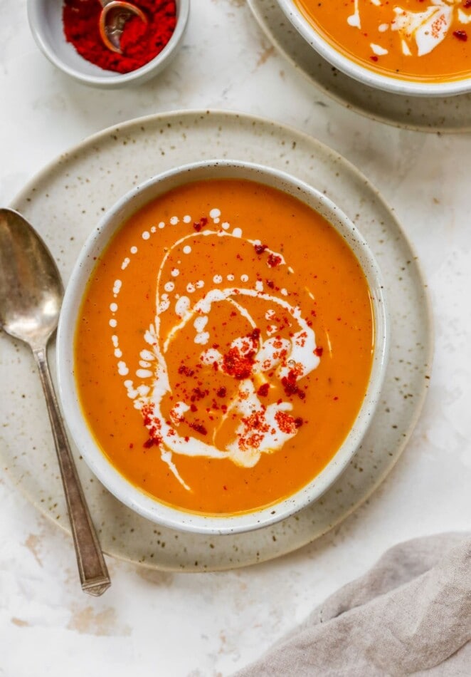 A bowl of sweet potato soup served on a plate with a metal spoon.