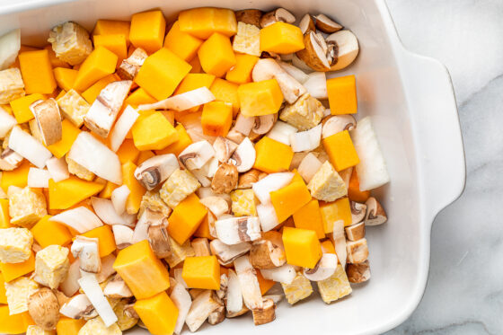 Tempeh, butternut squash, onion, and mushrooms tossed in a baking dish.