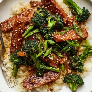 Bowl with rice topped with teriyaki tempeh and broccoli and sesame seeds. A fork is in the bowl.