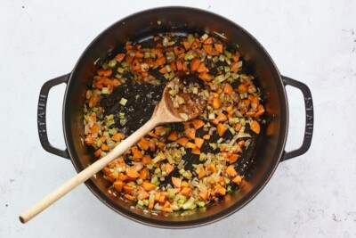 Veggies being mixed around with a wooden spoon in a cast iron dutch oven.