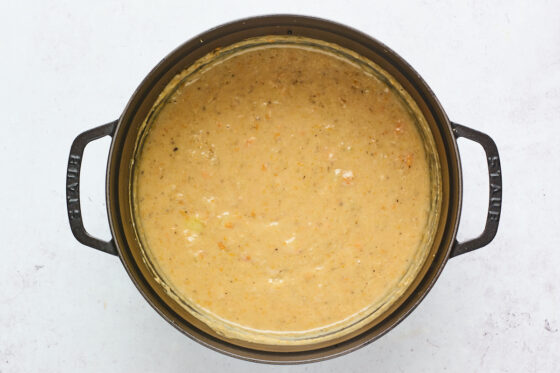 Vegan potato soup after it has been blended with an immersion blender in a cast iron dutch oven.