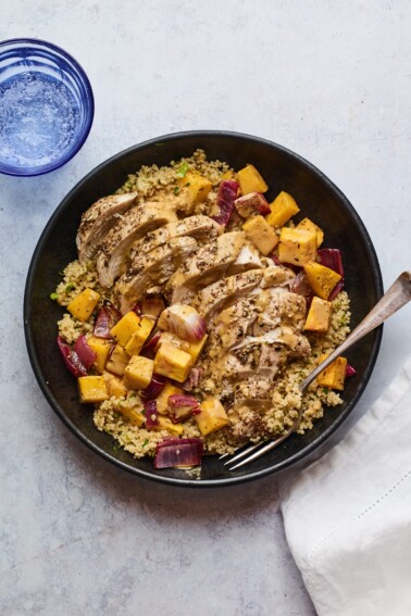 A plate of Za'atar chicken and vegetables over a bed of herbed couscous. A silver fork rests on the plate.