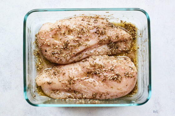 A shallow glass dish with chicken breasts soaking in marinade.