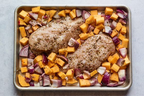 A sheet pan with seasoned chicken breasts and vegetables, ready to be roasted.