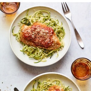 Two plates of chicken parmesan served over zucchini noodles.