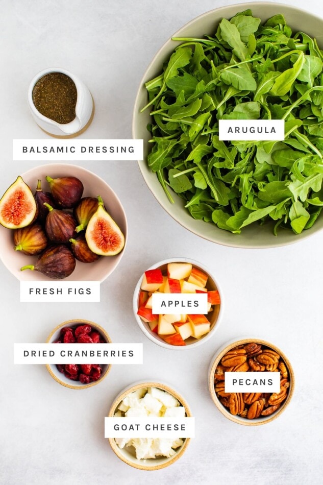 Ingredients measured out to make a fig salad: arugula, balsamic dressing, fresh figs, apples, dried cranberries, goat cheese and pecans.