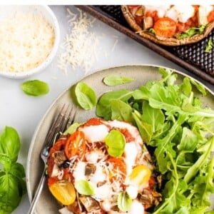 Overhead shot of a portobello mushroom pizza plated with arugula. A ramekin of cheese is in the top left corner and a silver fork rests on the plate.