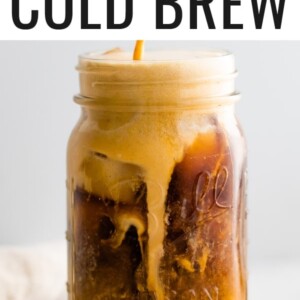 A mason jar with cold brew coffee and pumpkin cream being poured in to the top. The cream is mixing in with the cold brew.