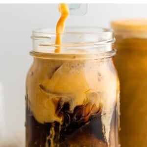 A mason jar with cold brew coffee and pumpkin cream being poured in to the top. The cream is mixing in with the cold brew.