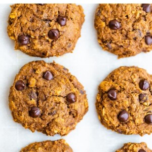 A close up of pumpkin oatmeal cookies, fresh from the oven. The cookies are resting on a sheet of parchment paper.