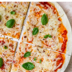 A close up overhead shot of a tortilla pizza. A ramekin of cheese is in the bottom right corner of the image.