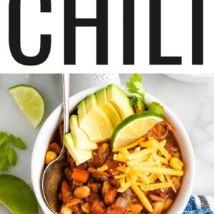 An overhead shot of a bowl of vegetarian chili, topped with avocado, shredded cheese, and a lime wedge.