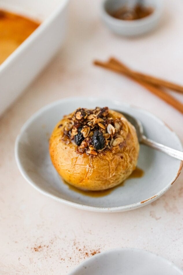 A baked apple with toppings served in a small dish with a silver spoon.