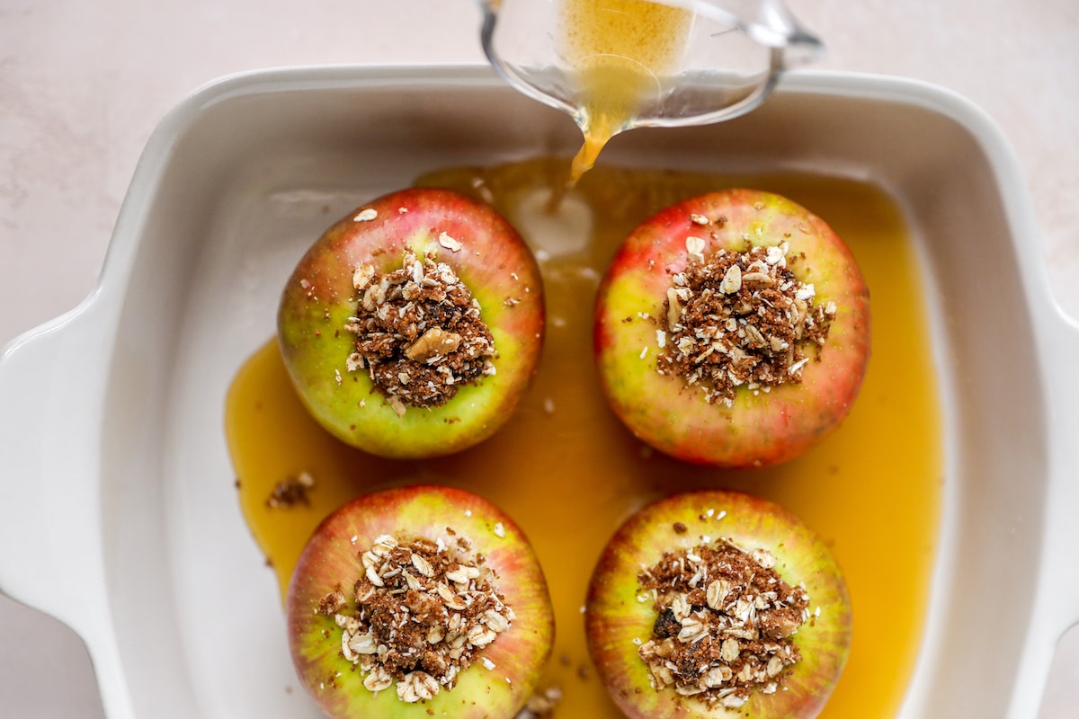 Warm apple cider poured into a rectangular baking dish holding 4 apples.