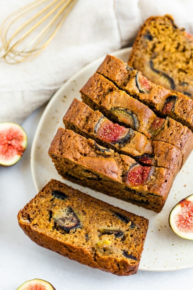 An overhead shot of a loaf of sliced fig bread on a plate. There is a slice lying horizontal where you can see the figs inside the bread.