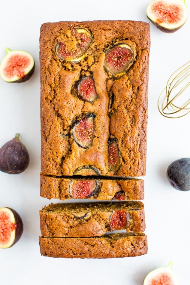 An overhead shot of Fig Bread. 3 slices have been cut but remain next to the loaf. There are additional figs surrounding the loaf.