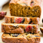 A close up of 3 slices of fig bread resting on top of each other. The remaining loaf is in the background.