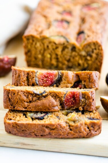 A close up of 3 slices of fig bread resting on top of each other. The remaining loaf is in the background.