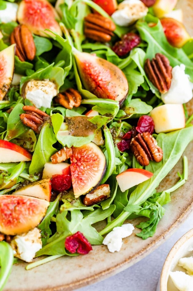 A close up of figs, pecans, apple chunks, and dried cranberry on a bed of arugula.