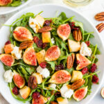 An overhead shot of a bowl of fig salad with a white wine glass next to it.